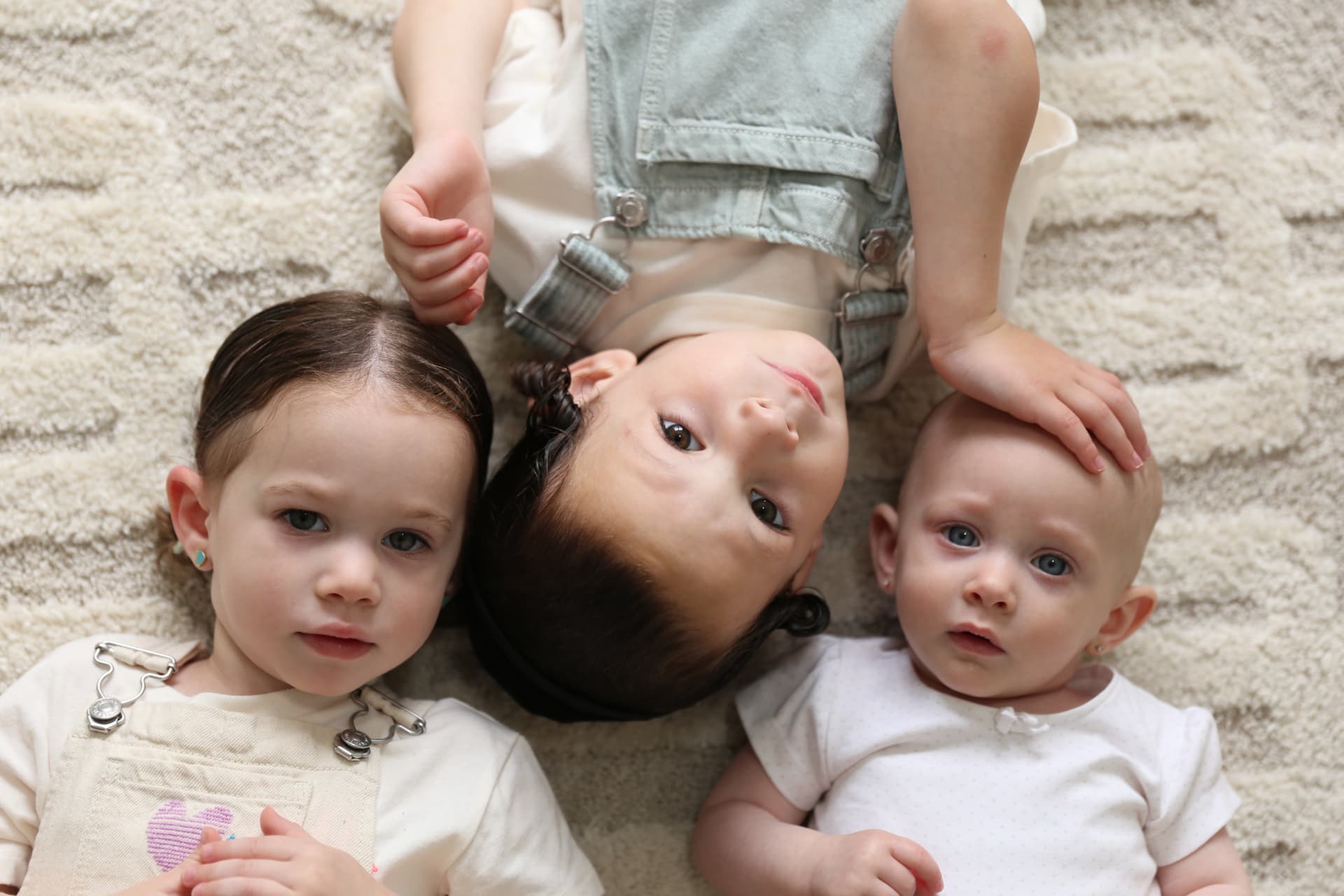 Three siblings lying head to head on the living room rug